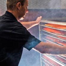 connemara-smokehouse-view-of-graham-looking-at-salmon-in-a-smoker-surrounded-by-wood-smoke